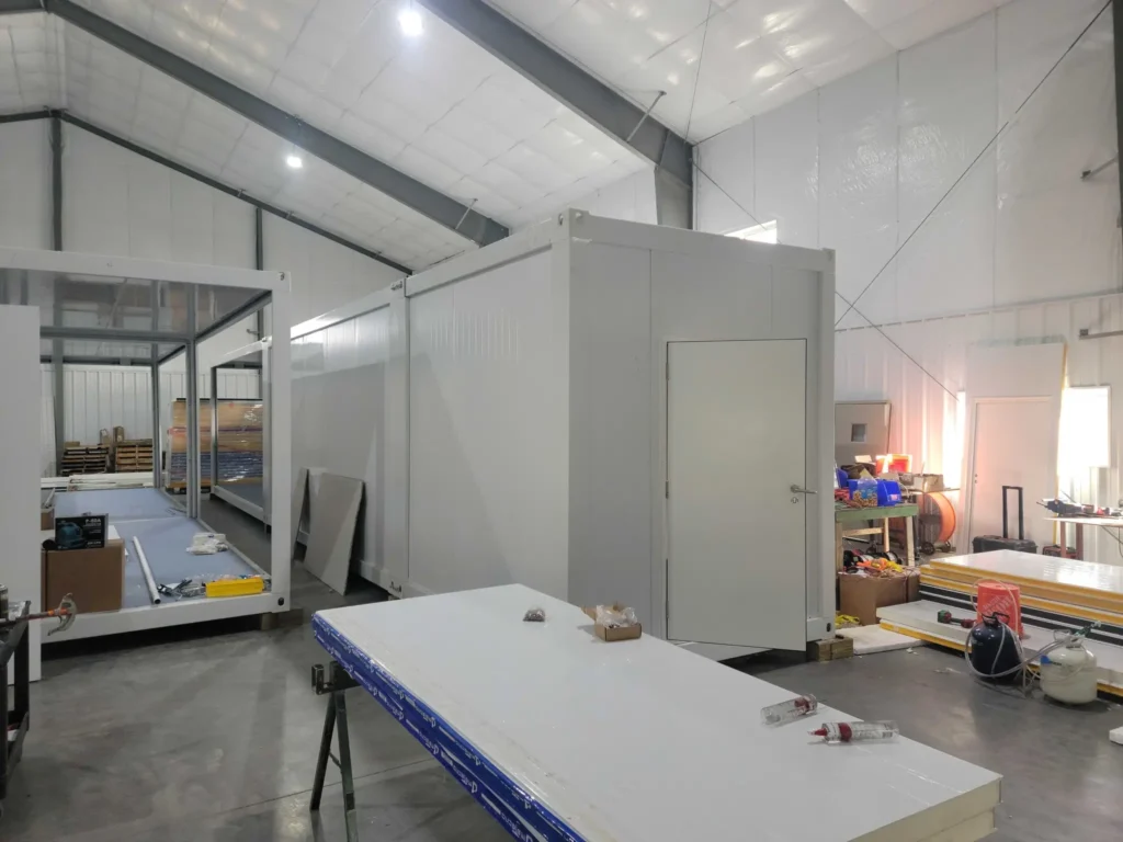 White modular prefabricated container unit under assembly inside warehouse.