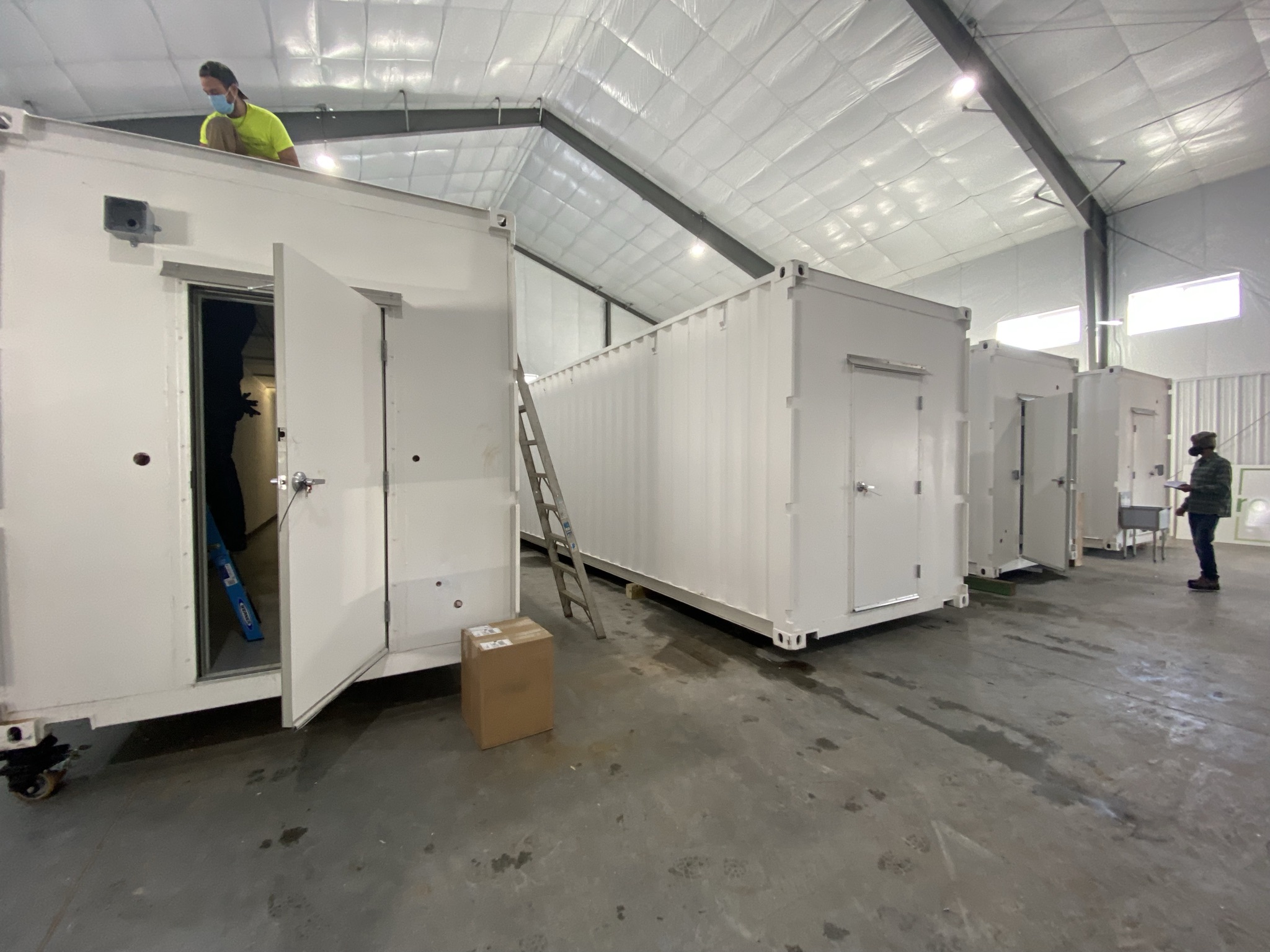 Workers assembling large white modular containers inside spacious warehouse.
