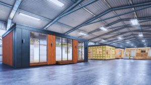 Modern modular home sections under construction in climate-controlled factory with metal roof and large windows, showing precision manufacturing process