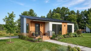 Modern 500 sq ft modular home with wood and white panel exterior, a covered porch, and landscaped yard surrounded by trees.