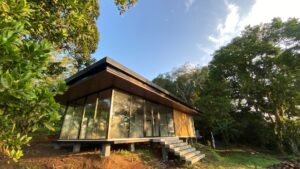 Modern modular home with large glass windows on a raised foundation among trees, illustrating what buyers should know about modular home warranties.